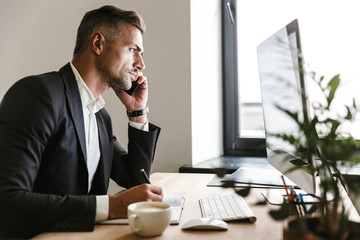 Wall Mural - image of successful businessman talking on cell phone while working on computer in office