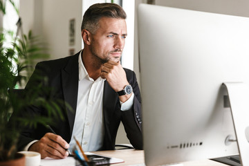 Wall Mural - image of confident businessman working in office and looking on computer