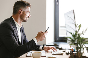 Wall Mural - portrait of successful businessman using mobile phone while working on computer in office