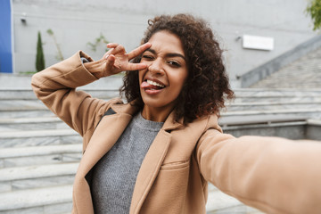 Wall Mural - Cheerful young african woman wearing coat walking