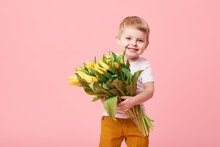 Adorable Smiling Child With Spring Flower Bouquet Looking At Camera Isolated On Pink. Little Toddler Boy Holding Yellow Tulips As Gift For Mom. Copy Space For Text 