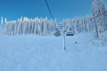 Chair lift in Poiana Brasov ski resort, Skiers and snowboarders enjoy the ski slopes in Poiana Brasov winter resort whit forest covered in snow on winter season