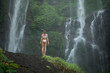 © South House Studio - back view of slim female in white bikini standing under great tropical fall,