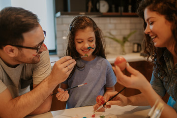 Close up of a cheerful family at the kitchen table. Easter time fun:painting eggs and their smiling faces.