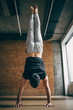 Young man doing yoga handstand in big bright training gym
