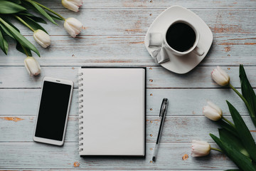 Wall Mural - Spring blanks of a freelancer's workplace with a bouquet of white tulips, a smartphone, an empty white bouquet and a Cup of coffee in his hands on wooden background