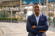 © Ranta Images - Young happy African businessman smiling with arms crossed in the city