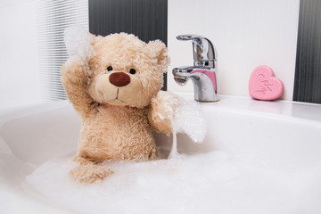 A cute teddy bear is sitting in the basin and washing. 