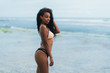 Sexy african american girl in swimwear resting on ocean beach. Young black skinned woman with curly hair stands on seashore