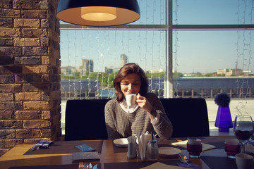 pretty young woman sitting in a cafe with cup of tea