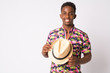 Portrait of happy young African tourist man smiling and holding hat