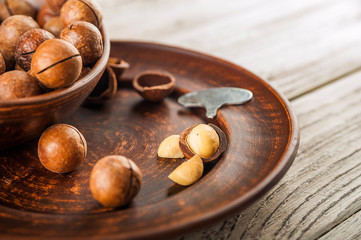 Macadamia nuts on a wooden plate on a white textural table close up and copy space