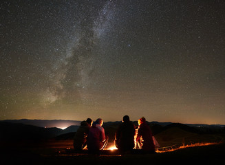 night summer camping in the mountains. back view group of four friends tourists sitting on a bench m