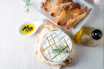 Wall Mural - Baked camembert cheese. Fresh Brie cheese and a slice on a wooden board with nuts, honey, rosemary, baguette bread grilled toasts and leaves. Brie type of cheese. Italian, French cheese.