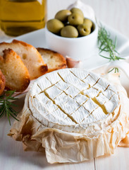 Wall Mural - Baked camembert cheese. Fresh Brie cheese and a slice on a wooden board with nuts, honey, rosemary, baguette bread grilled toasts and leaves. Brie type of cheese. Italian, French cheese.