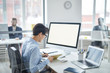 © Seventyfour - Young businesswoman in blue shirt making notes in notebook while sitting by desk in front of computer monitor