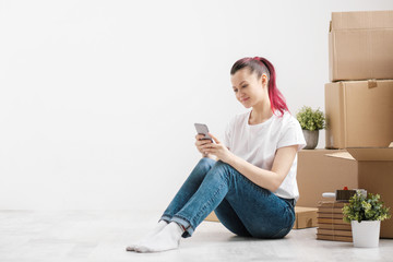 Wall Mural - Young beautiful girl with colored hair in a white T-shirt and jeans, talking on the phone and writes messages against the background of cardboard boxes and things.