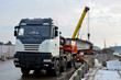© MaxSafaniuk - A crane unloads a long concrete slab from a truck at a construction site. Workers unload reinforced concrete panels