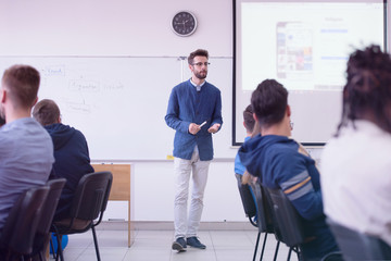 Group of students study with professor in modern school classroom. Male professor explain to students and interact with them, helping a students during class.