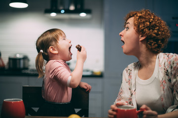 Mom and daughter have dinner in the evening at home in the kitchen.