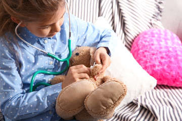 Poster - Cute child imagining herself doctor while playing with stethoscope on sofa in living room