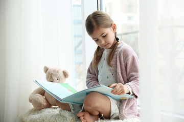 Sticker - Cute little girl reading book near window at home