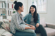 © PR Image Factory - Close up photo of two asian young people excited tell speak news fresh gossips gladly smiling wear jeans sit on comfy sofa in living room. girls chatting talking on couch in bright room at home laugh