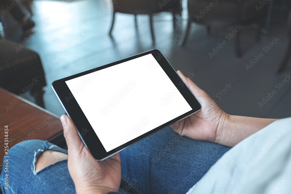 Mockup image of a woman sitting and holding black tablet pc with blank white desktop screen horizontally - obrazy, fototapety, plakaty 