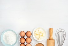 Baking Ingredients And Kitchen Utensils On White Background. Chicken Eggs, Butter, Sugar, Flour, Rolling Pin And Whisker. Cooking, Baking, Pastry Or Cookie Dough Ingredients