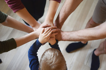 Stack of family people hands - father with children on light brown wooden texture laminate floor background indoors. Family business, teamwork and unity concept.