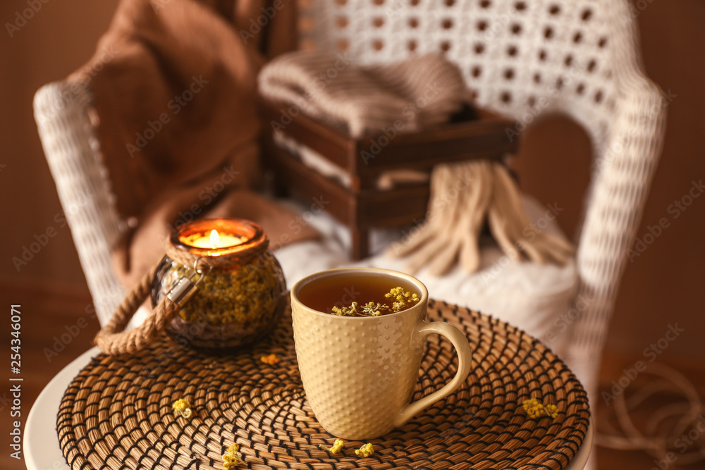 Cup of hot tea and holder with candle on wicker mat