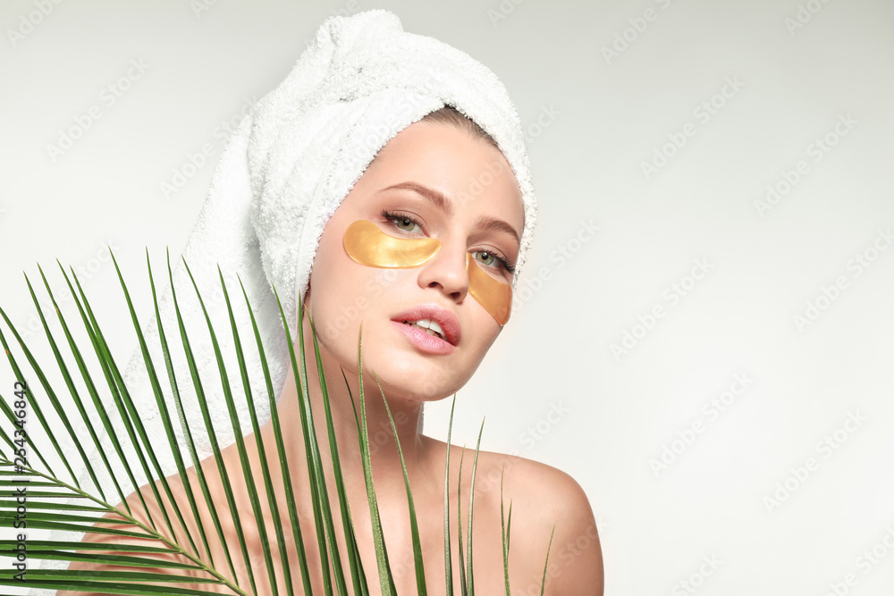 Young woman with under-eye patches and tropical leaf on white background