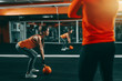 © dusanpetkovic1 - Young Caucasian sporty woman in orange shirt and ponytail lifting kettlebell in gym at night while her personal trainer looking at her. In background mirror. Excuses don't burn calories.
