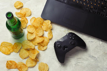 Wall Mural - Laptop, Gamepad, Potato chips, Bottle of Beer on a light stone background. Concept of computer games and leisure