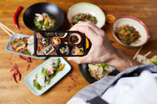 Top View Closeup Of Unrecognizable Man Taking Picture Of Asian Food Dishes, Copy Space