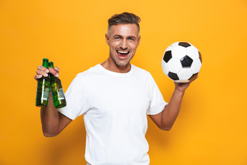 Poster - Image of european man 30s in white t-shirt drinking beer and holding soccer ball while standing isolated