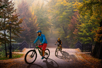 Poster - Couple cycling in golden shine trail foggy scene in the park, woman and man riding on bike the morning sun shining through the trees, blue sky in background.