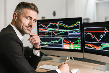 Wall Mural - Portrait of confident businessman sitting in office and working with digital graphics on computer