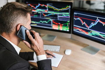 Wall Mural - Portrait of adult businessman speaking on cell phone while working with digital graphics on computer in office