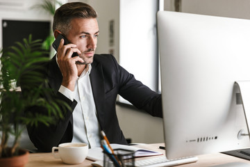 Wall Mural - image of smart businessman talking on cell phone while working on computer in office