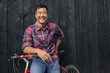 © mavoimages - Smiling young man with a bike against a city wall