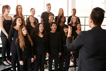 Male And Female Students Singing In Choir With Teacher At Performing Arts School