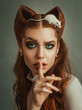 © kharchenkoirina - cute lady with cat ears of red hair and bright green makeup, girl asks for silence puts finger to lips, little white mouse sits on head. creative work of makeup artist and hairdresser, art processing