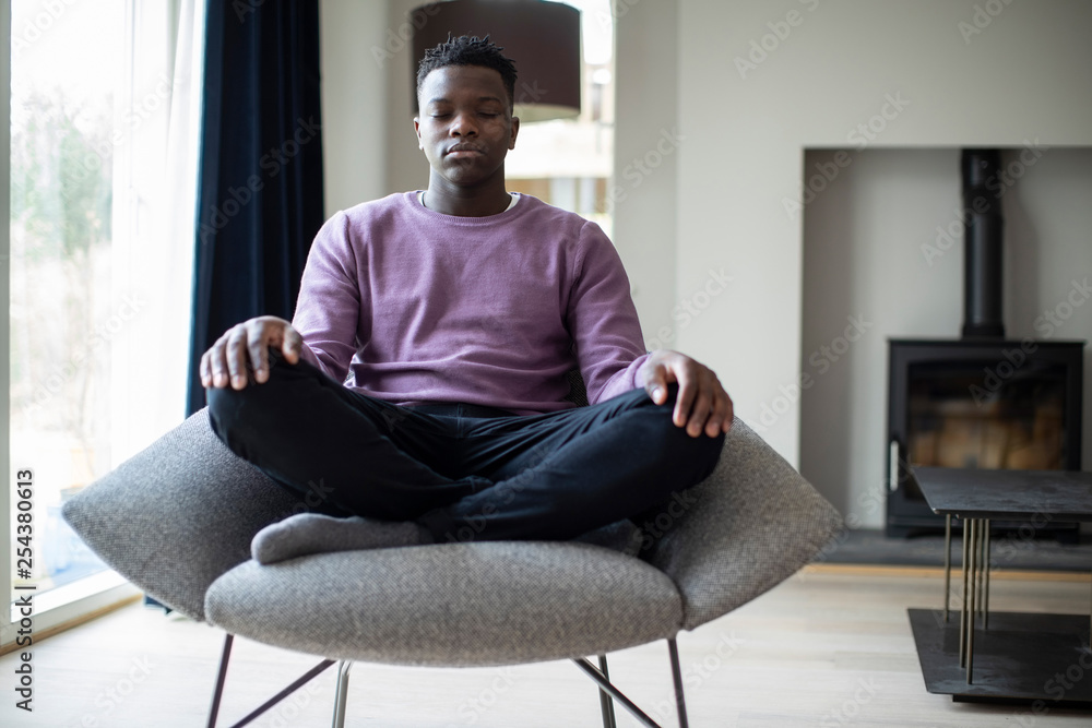 Close Up Of Peaceful Teenage Boy Meditating Sitting In Chair At Home - obrazy, fototapety, plakaty 