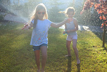 Child Playing With Garden Sprinkler. Kids Run And Jump. Summer Outdoor Water Fun In The Backyard. Child Playing With Garden Sprinkler. Kids Run And Jump. Summer Outdoor Water Fun In The Backyard