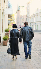 A loving couple walking the streets of old Riga, Latvia. A woman is wearing leather jacket and high heels, man is wearing leather jacket. They are holding hands.