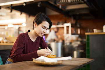 Side view portrait of young woman eating Asian food in restaurant, copy space