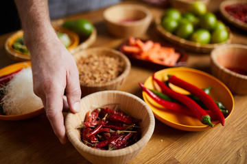 Wall Mural - Close up of unrecognizable man holding chili peppers bowl while cooking spicy food, copy space