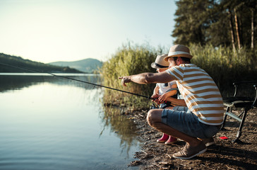 Wall Mural - A mature father with a small toddler son outdoors fishing by a lake.