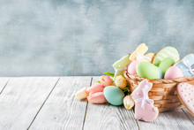 Easter Greeting Card Background With Pastel Colored Eggs And Homemade Cookies Shaped In Eggs And Bunnies Rabbits. With A Basket, Tulips, Rustic Wooden Table, Copy Space Top View Banner